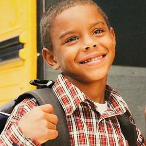 Young boy happy to get on school bush holding backpack strap